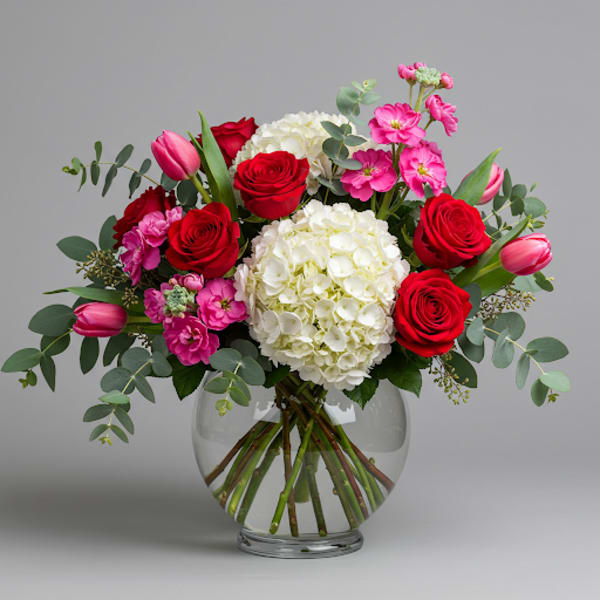 Bouquet of red roses, white hydrangeas, and pink tulips in a glass vase
