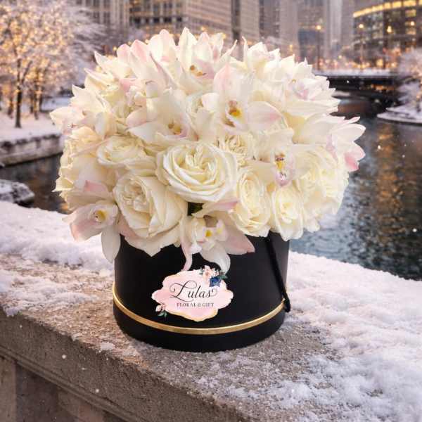 White roses and pale orchids in a black hatbox