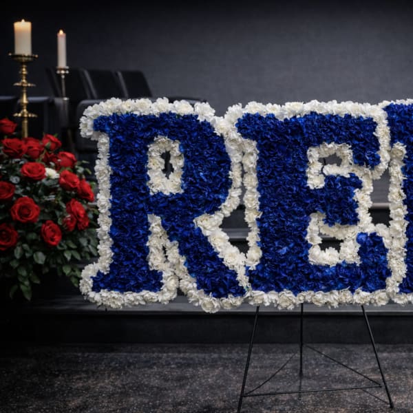 Blue and white floral tribute spelling RED on a stand