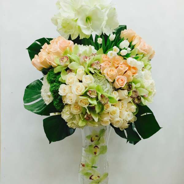 Tall bouquet of cream and peach flowers in a clear glass vase