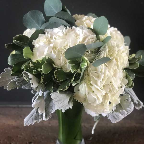 White hydrangea bouquet in a green glass vase with eucalyptus