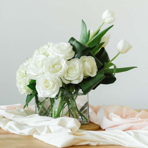 White roses and tulips arranged in a clear glass vase
