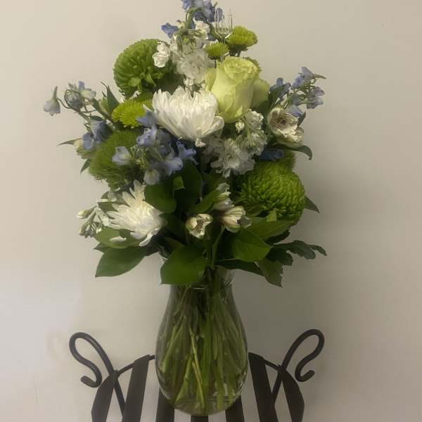 Bouquet of white, green, and blue flowers in a clear glass vase