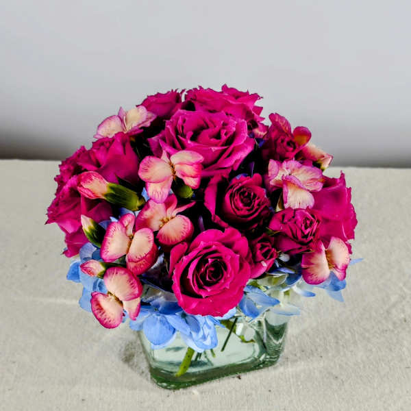 Pink rose bouquet in a square glass vase with blue flowers