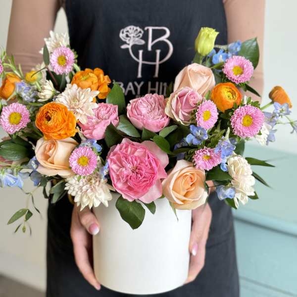 Mixed bouquet of pink, peach, orange, and blue flowers in a white box