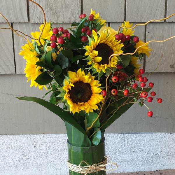 Sunflower bouquet in a glass vase with red berry accents