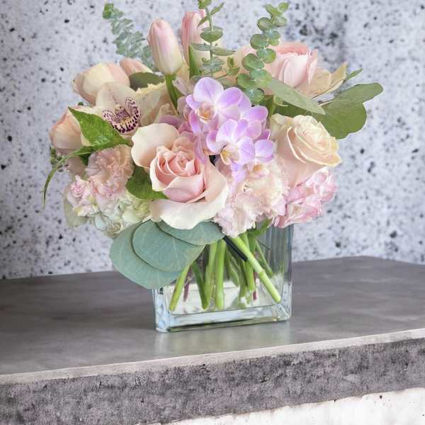 Pastel bouquet of roses, tulips, and orchids in a clear glass vase