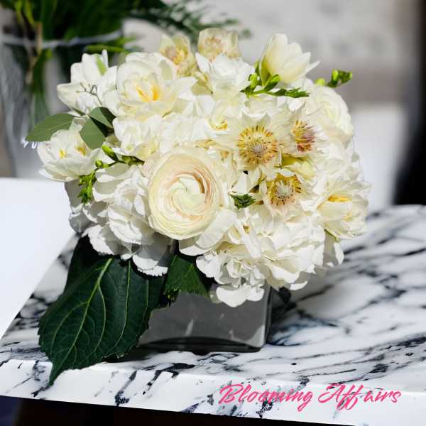 White floral bouquet in a square vase on a marble surface
