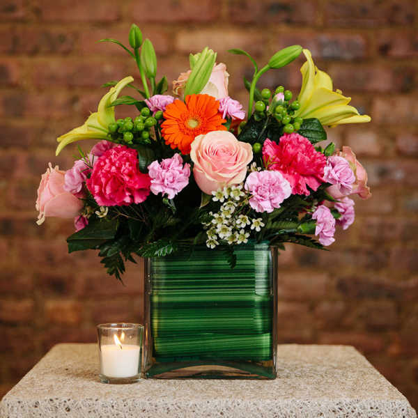 Mixed bouquet in a green glass vase with a small candle beside it
