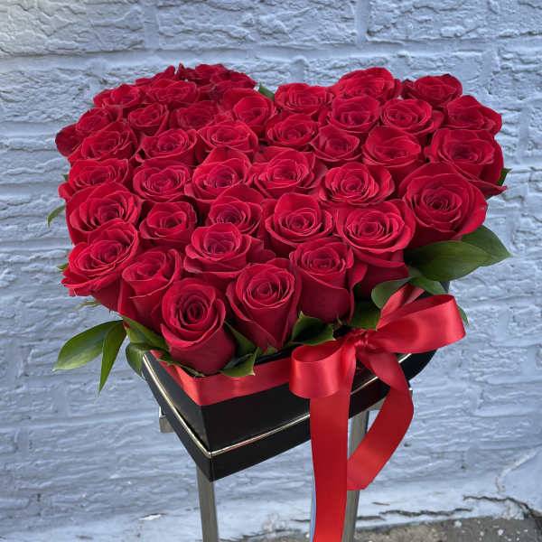 Heart-shaped arrangement of red roses with a red ribbon on a black stand