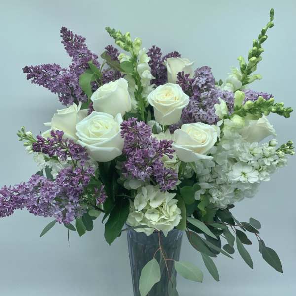 White roses and purple lilacs arranged in a clear glass vase