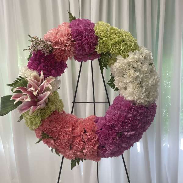 Circular floral wreath on a black stand with pink, purple, green, and white blooms