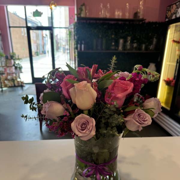 Pink and lavender roses arranged in a glass vase with a purple ribbon