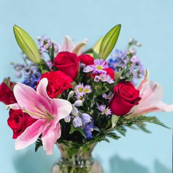 Bouquet of pink lilies, red roses, and purple daisies in a glass vase