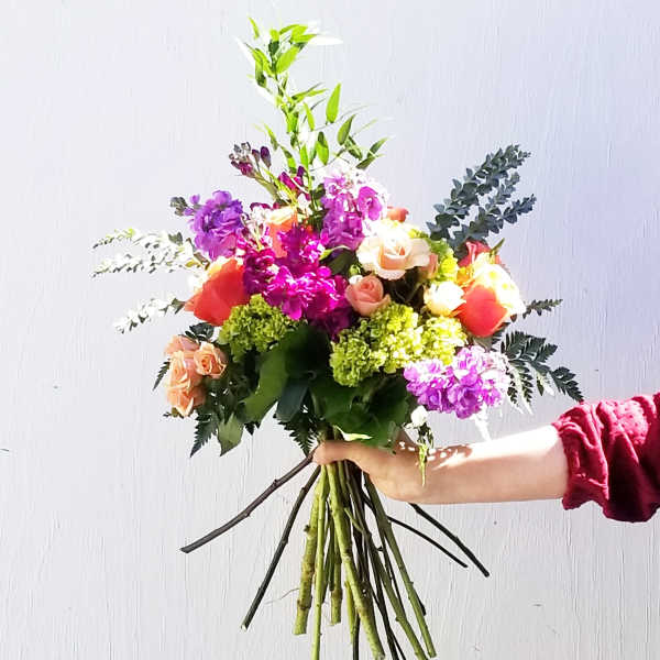 Handheld bouquet of mixed pink, purple, and peach flowers