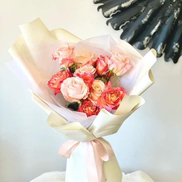 Bouquet of pink and peach roses wrapped in cream paper