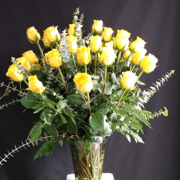 Yellow roses arranged in a clear glass vase with eucalyptus foliage