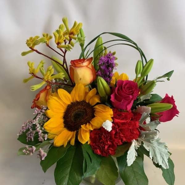 Mixed bouquet with a sunflower, roses, lilies, and carnations in a glass vase