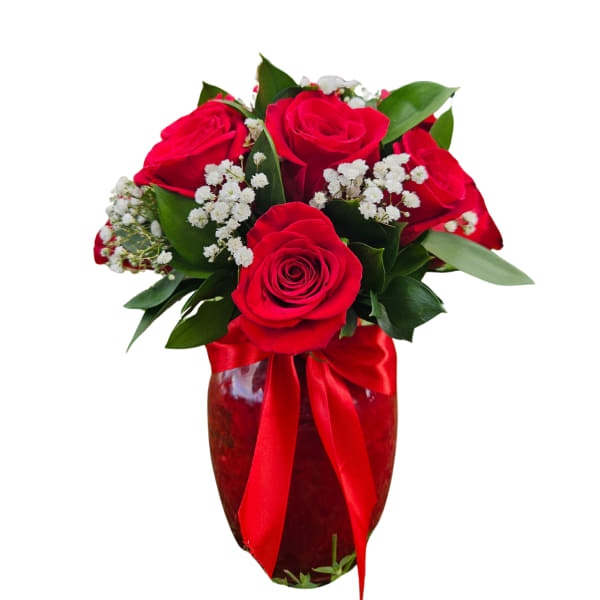 Red roses arranged in a glass vase with white filler flowers and a red ribbon