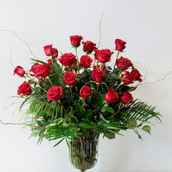 Red roses arranged in a clear glass vase with greenery