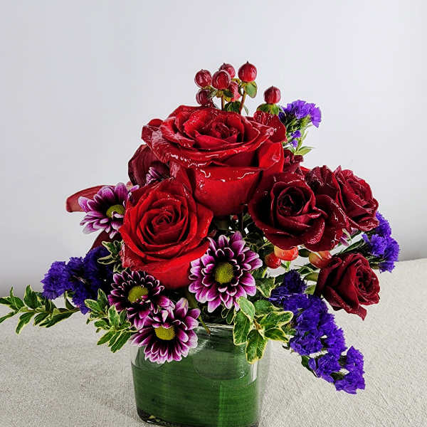 Red roses and purple daisies arranged in a square glass vase