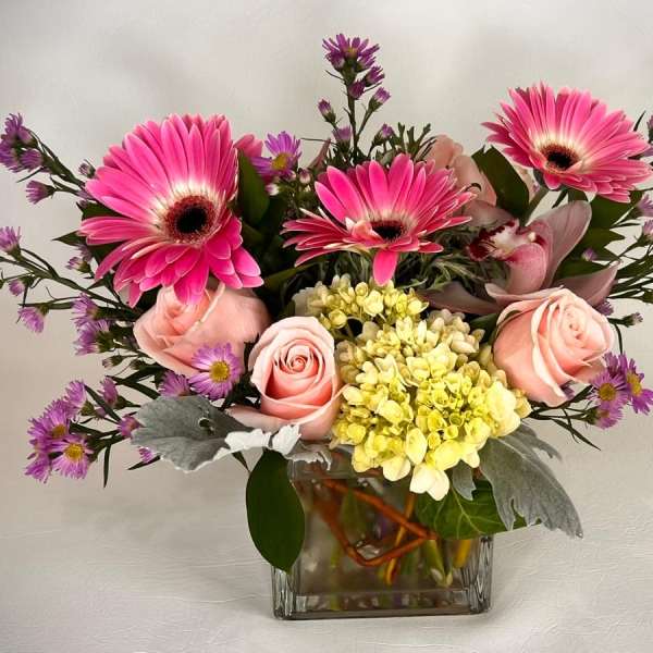 Pink gerbera daisies and roses in a square glass vase