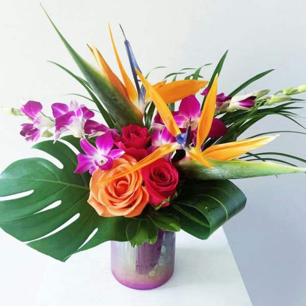 Tropical bouquet with roses, orchids, and bird of paradise in a glass vase