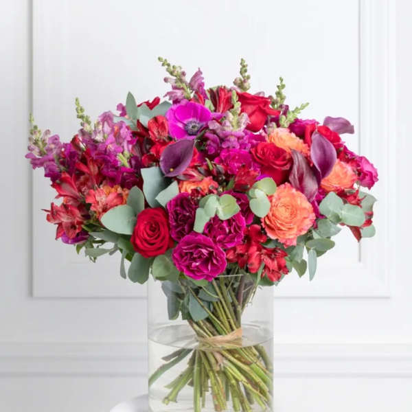 Bright mixed bouquet of pink, red, and orange flowers in a clear glass vase