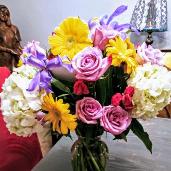 Bouquet of pink roses, yellow daisies, and white hydrangeas in a glass vase