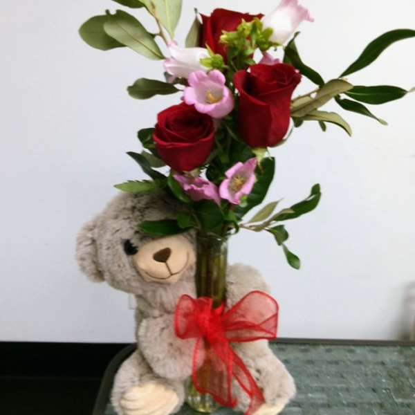 Red roses and pink flowers in a glass vase with a teddy bear