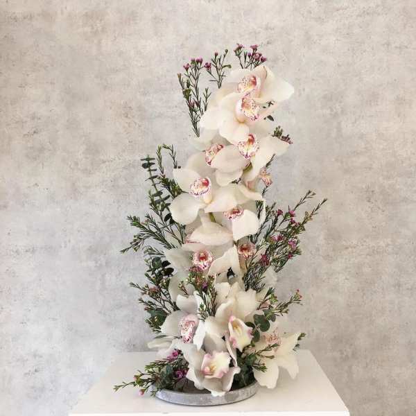 Tall white orchid arrangement with small pink accent flowers in a round base