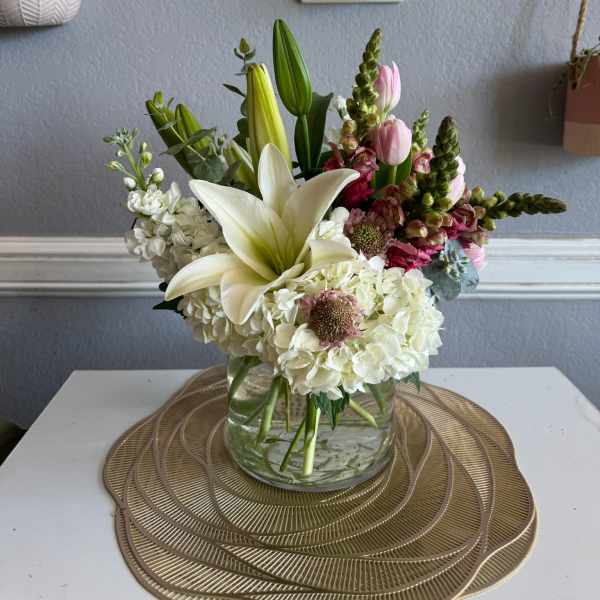 Mixed bouquet with white lilies, hydrangeas, and pink blooms in a glass vase