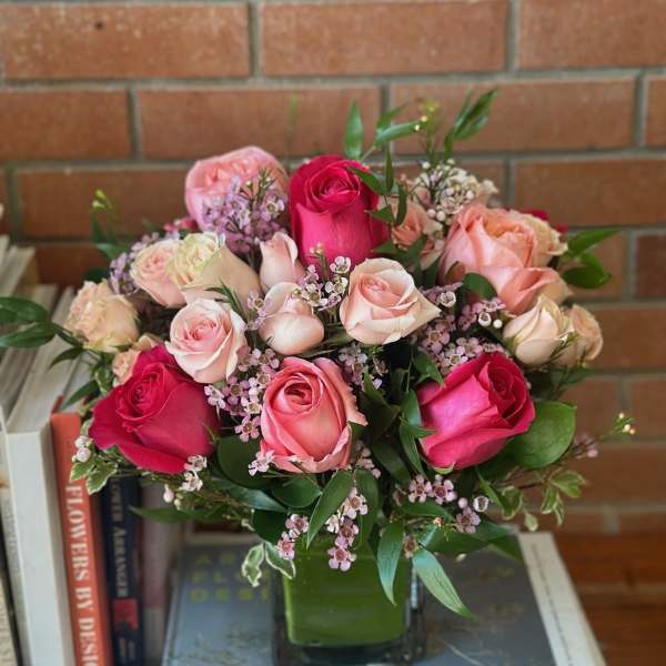Rounded arrangement of pink and cream roses with tiny pink blossoms in a square glass vase