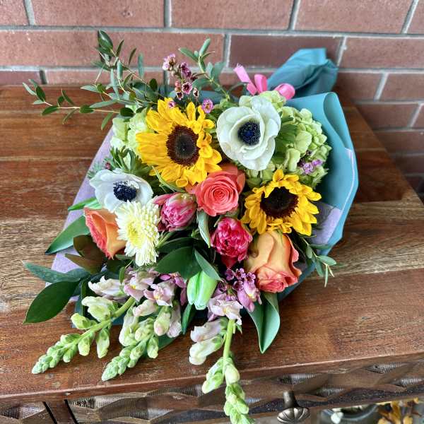Mixed bouquet with sunflowers, roses, and white anemones wrapped in blue paper
