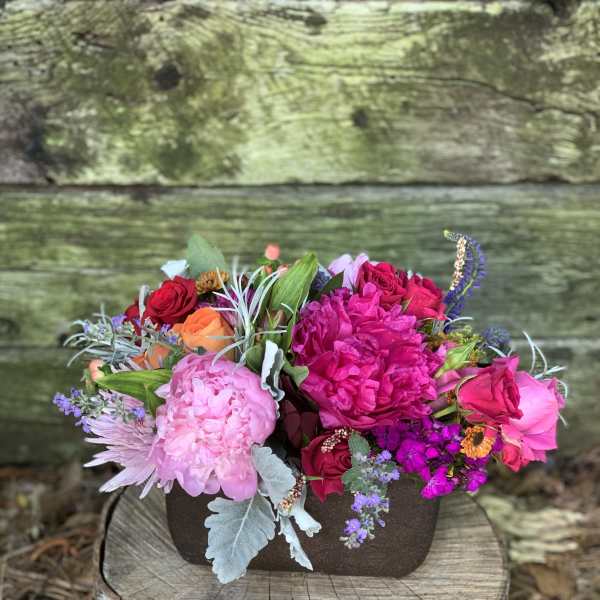 Mixed bouquet of pink, red, and orange flowers in a dark container