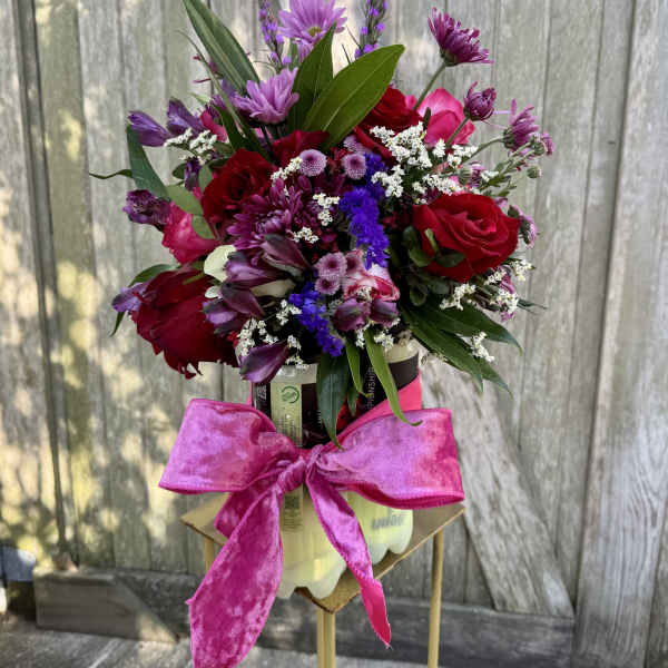 Mixed bouquet of red and purple flowers in a container with a pink bow