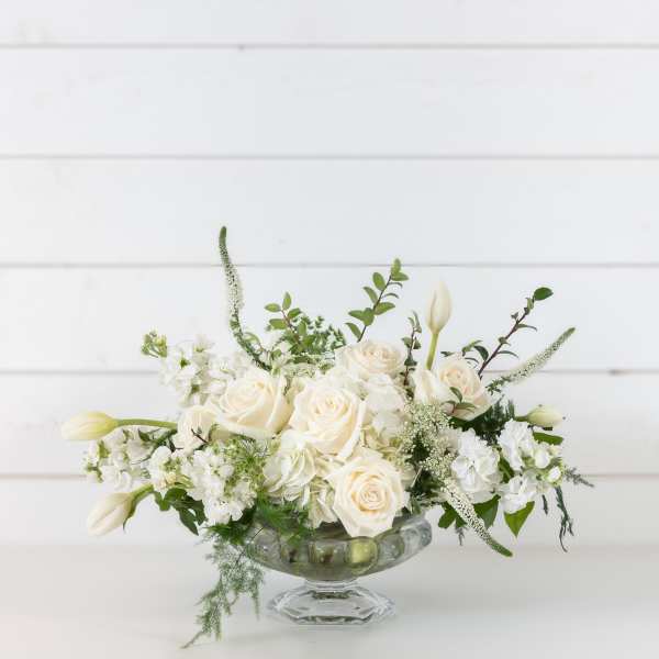 White roses and tulips arranged in a clear glass compote vase