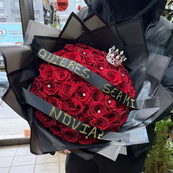 Large bouquet of red roses wrapped in black paper with a crown and glitter ribbon