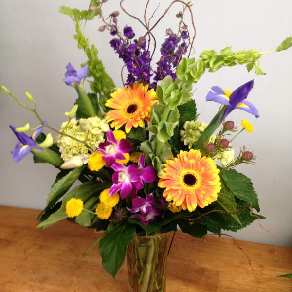 Colorful mixed bouquet in a clear glass vase with orange gerberas and purple blooms