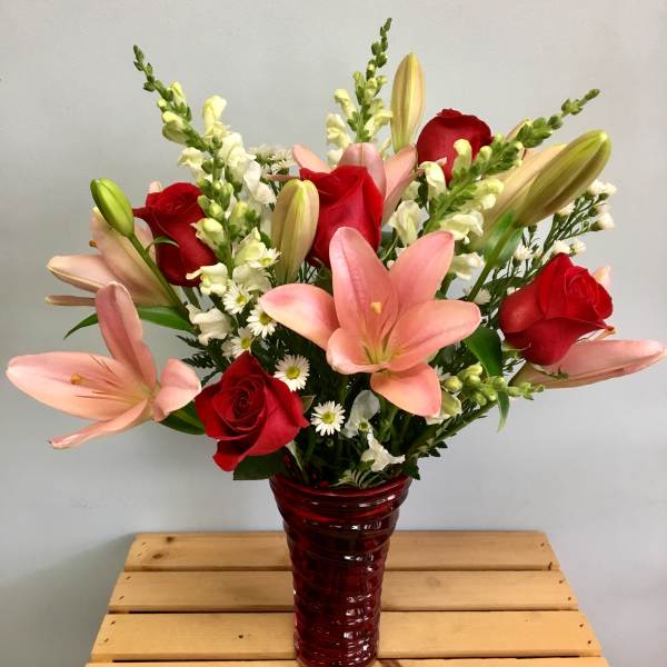Bouquet of pink lilies and red roses in a red glass vase