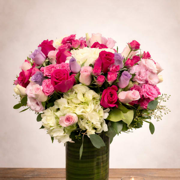 Pink and white rose bouquet in a glass vase beside a lit candle