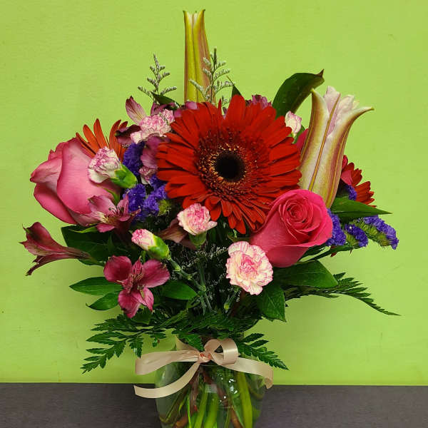 Mixed bouquet with pink roses, red gerbera daisies, and lilies in a glass vase