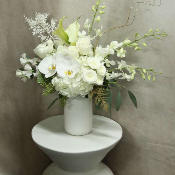White floral arrangement in a white vase with orchids and roses