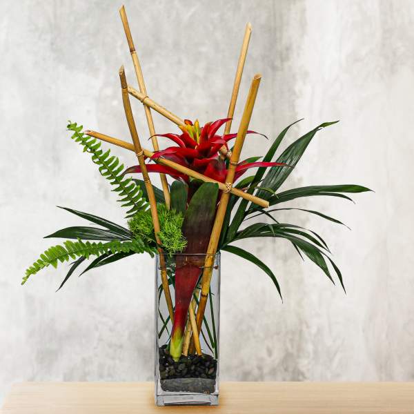 Red tropical flower arrangement in a tall glass vase with bamboo accents