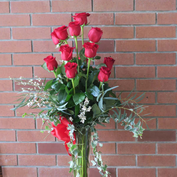 Tall vase arrangement of red roses with trailing greenery