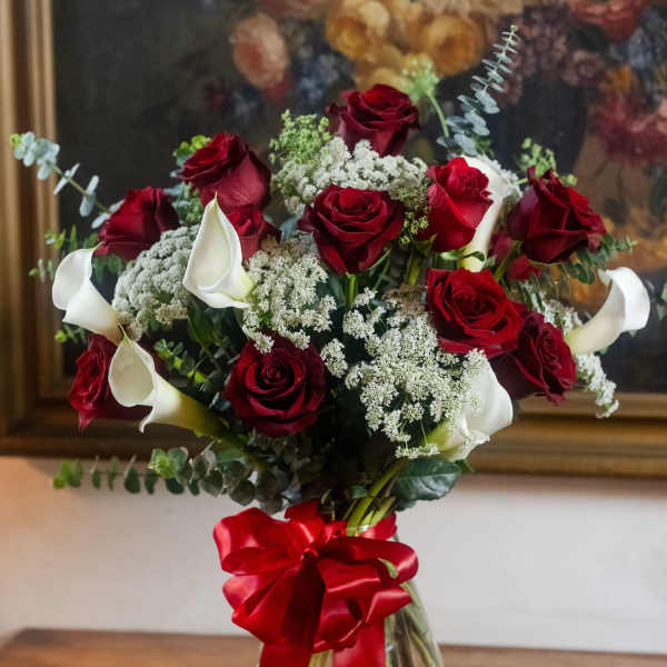 Bouquet of red roses and white calla lilies in a glass vase with a red ribbon