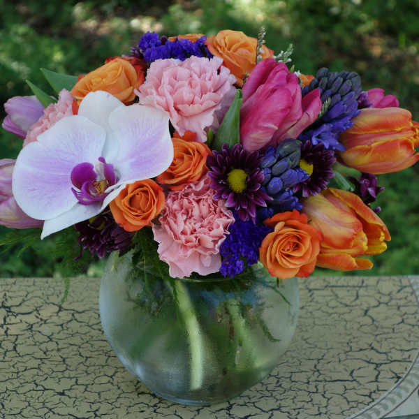 Colorful mixed bouquet with orchid, roses, tulips, and carnations in a round glass vase