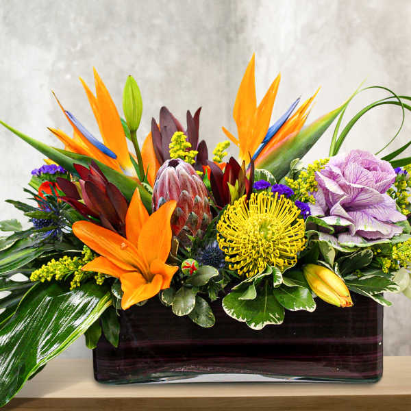 Tropical floral arrangement with orange and purple blooms in a rectangular vase