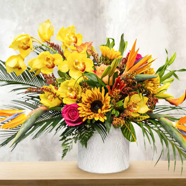 Tropical bouquet with yellow orchids, sunflowers, and bird-of-paradise in a white vase