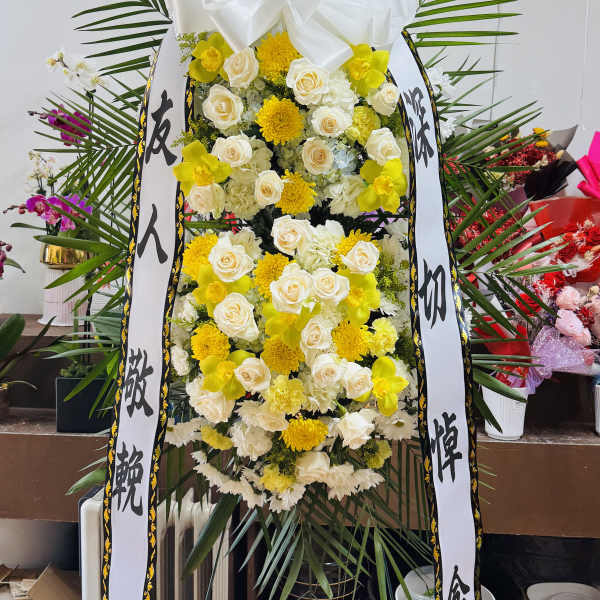 Tall funeral standing spray with white and yellow flowers and ribbon streamers